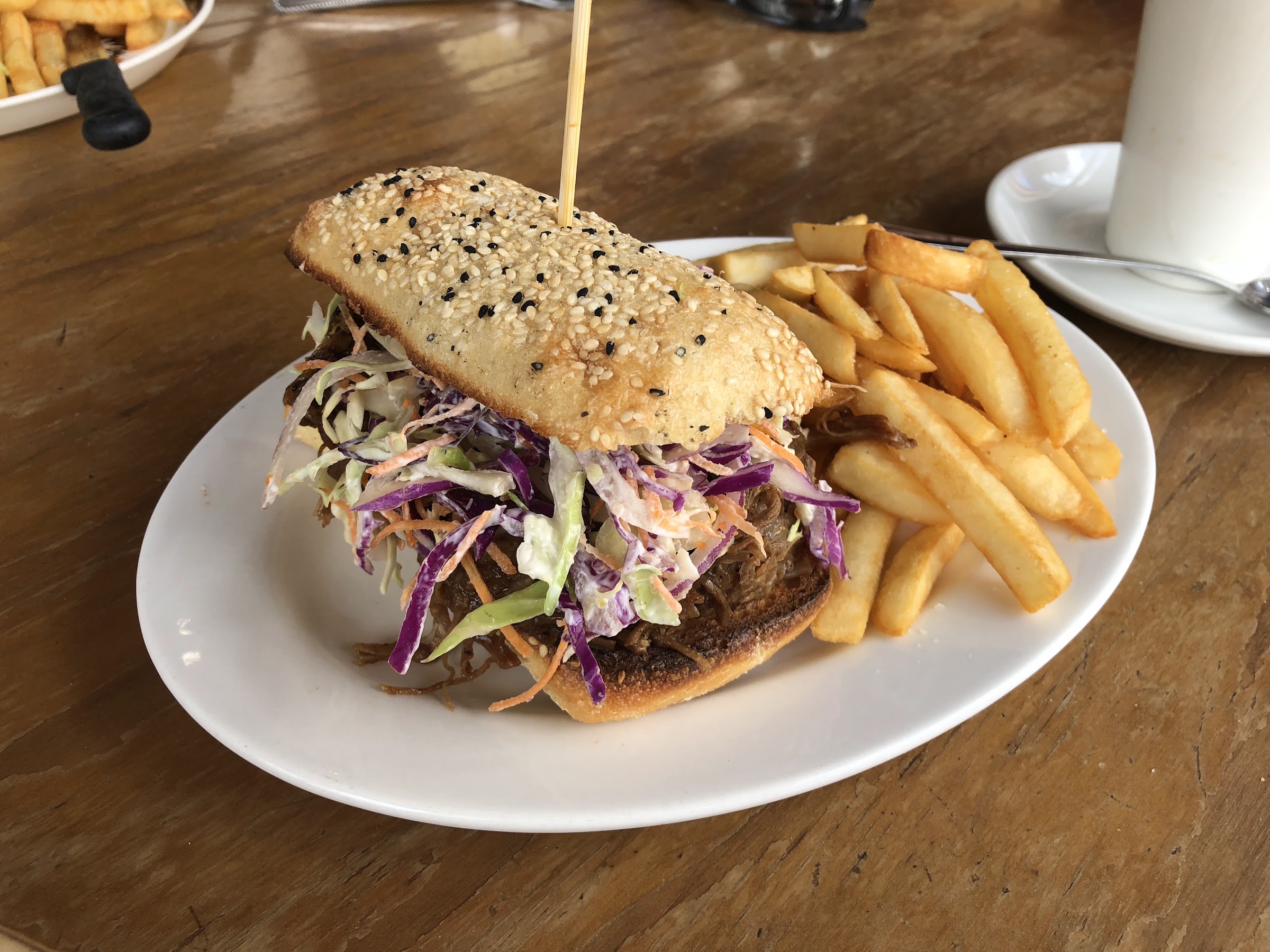 A pulled meat roll with slaw on a sesame bun, served with chips