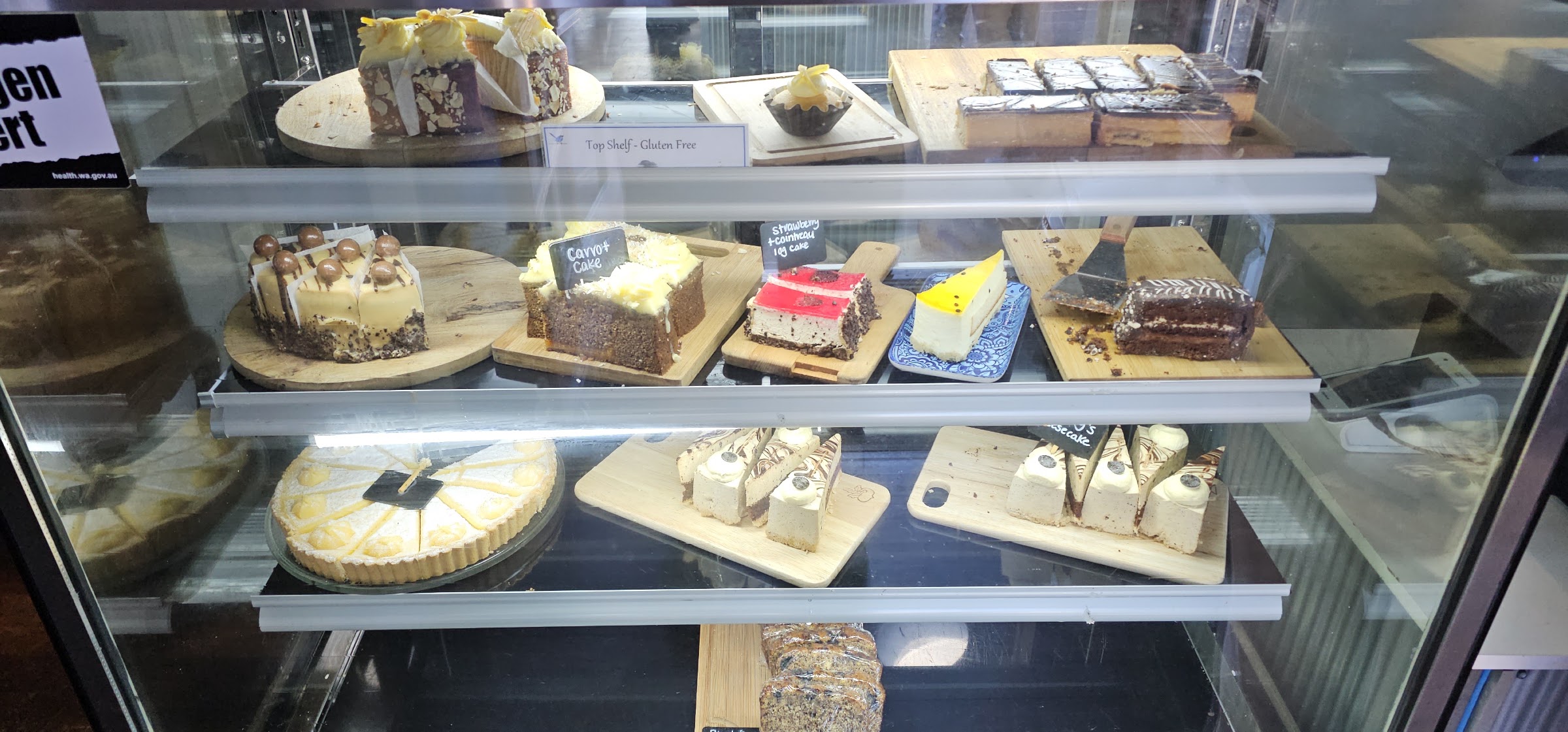 The cake cabinet at Blue Wren Café, with carrot cake, cheesecakes, a lemon tart and slices on timber boards