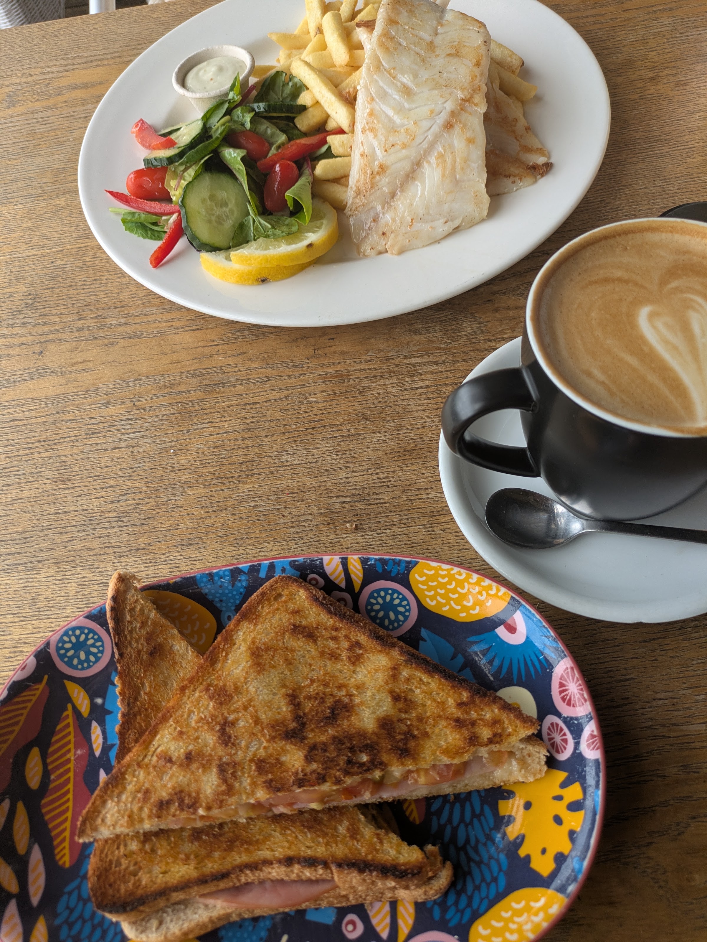 Grilled fish with chips and salad, a toasted sandwich and a latte